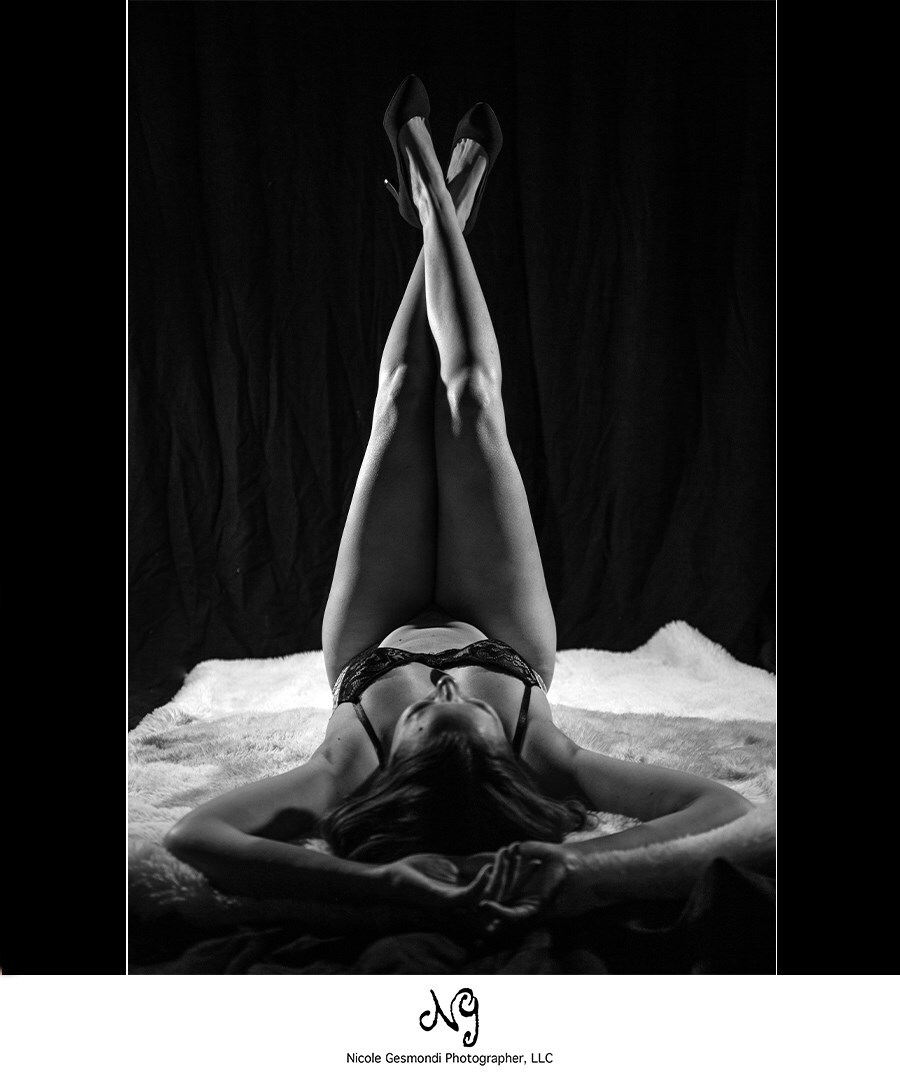 black and white boudoir photo of woman laying on back with legs in the air
