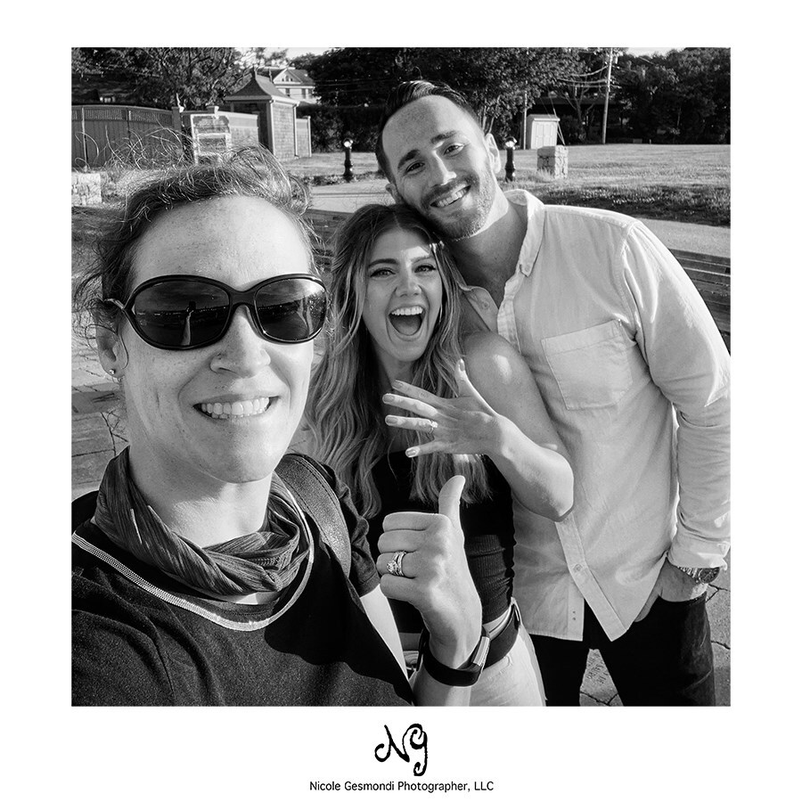 photographer poses with newly engaged couple